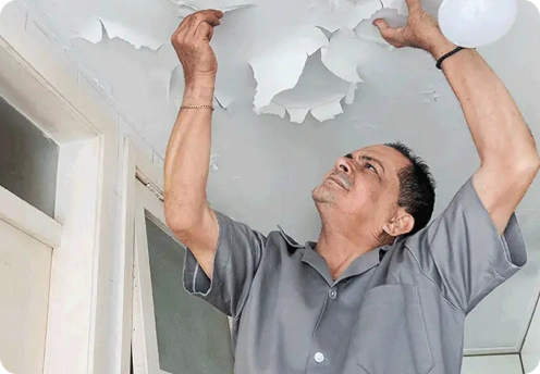 Hombre inspeccionando techo con pintura desprendida por goteras en Alcobendas, Madrid. Reparación de cubiertas y tejados.